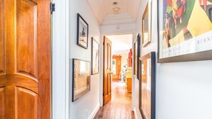 A hallway with wooden doors, framed pictures on the walls, and a view into another room.