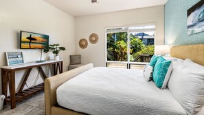 Ein Schlafzimmer mit Bett, Schreibtisch mit Topfpflanze, Blick ins Freie und einem Kunstwerk im Strandhausstil.