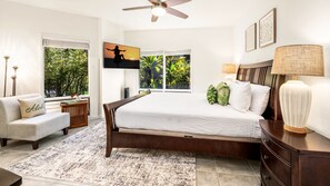 A bedroom with a large bed, a nightstand, a chair, a lamp, and a TV on the wall. - 🏖️Ocean Front Views | Central AC | 3 Complex Pools (Kailua Kona)