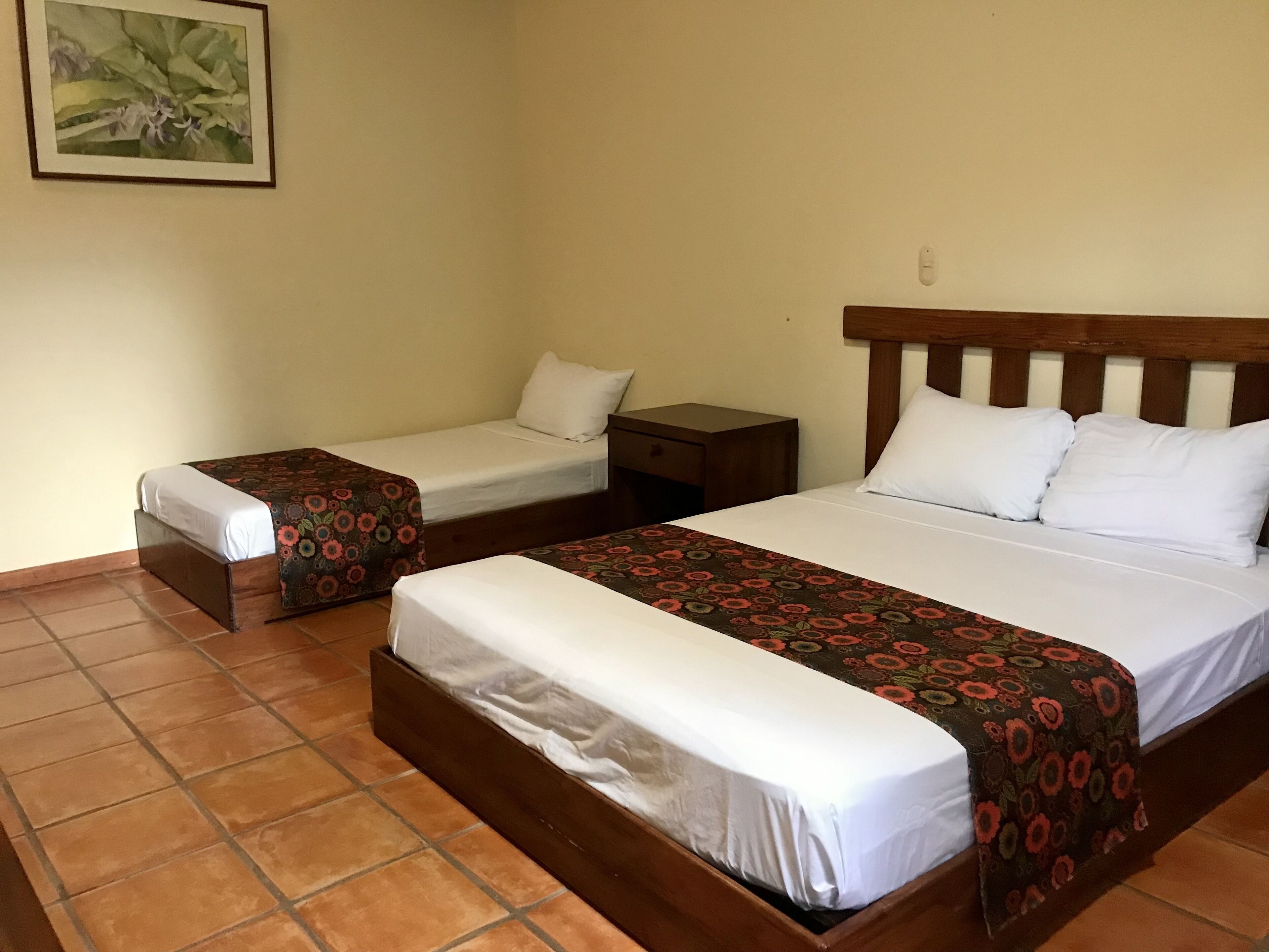 A hotel room with two single beds, a wooden headboard, a nightstand, and a wall-mounted painting.