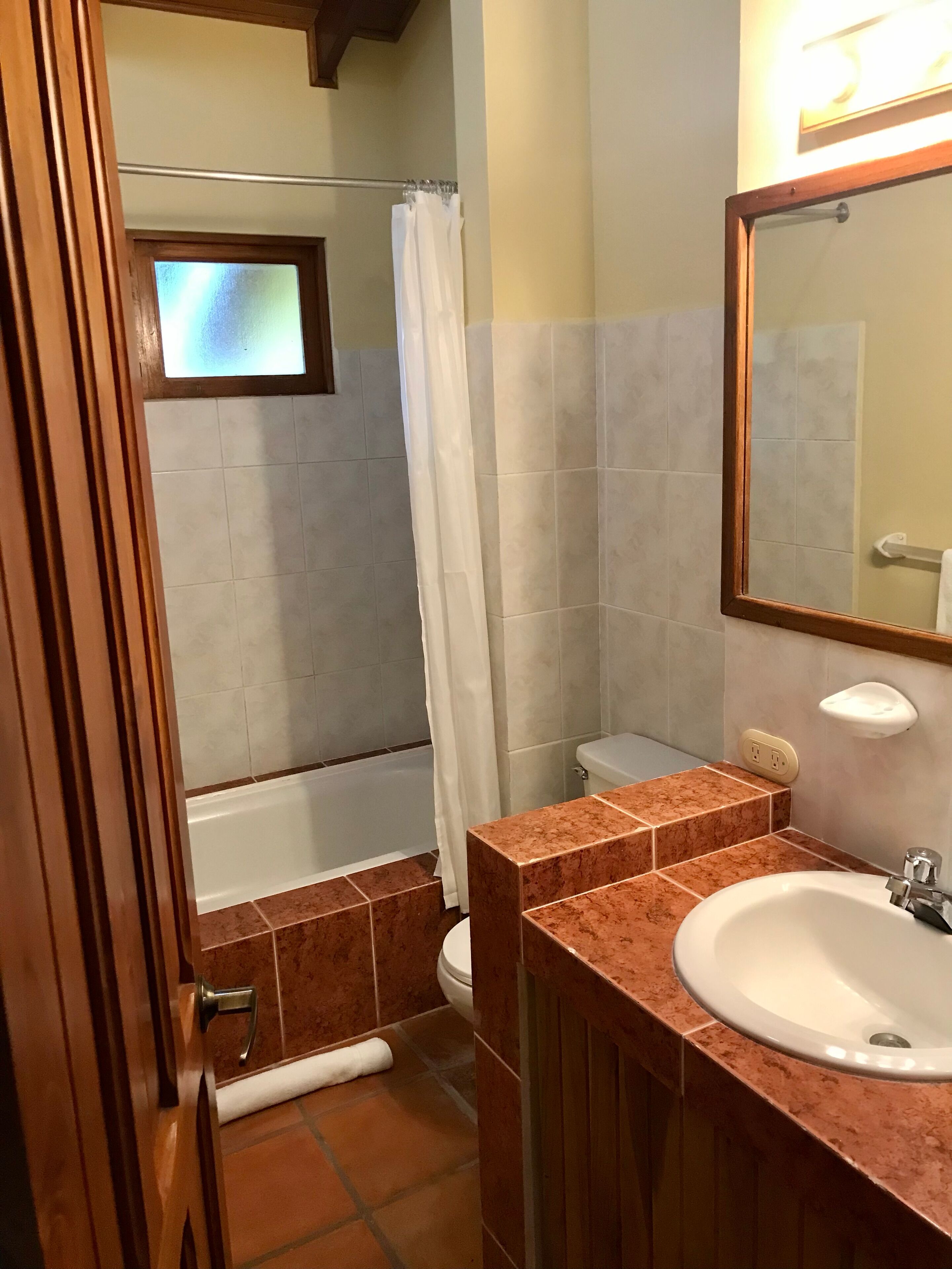 Une salle de bain avec un lavabo en marbre, des toilettes, une douche avec un rideau et un miroir.