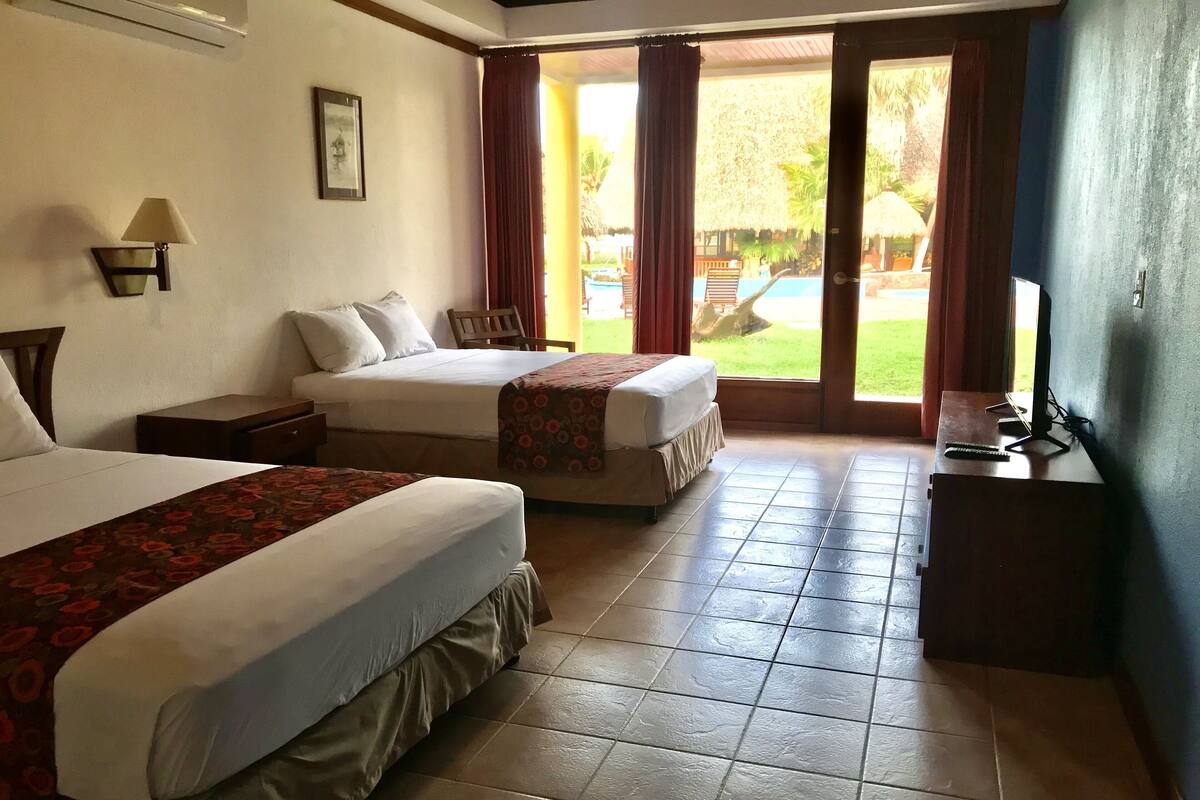 A hotel room with two beds, a desk, a chair, a TV, and a view of a pool.
