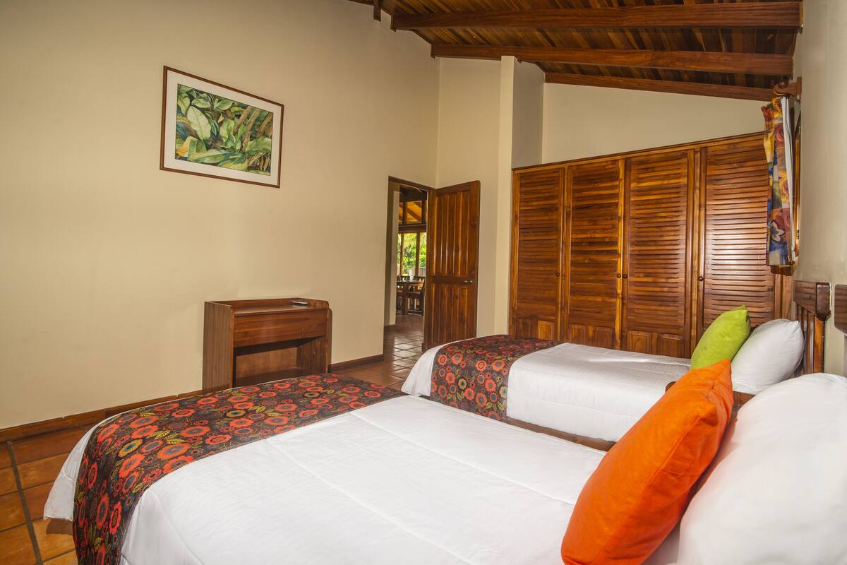 A hotel room with two beds, a wooden wardrobe, a wooden desk, and a framed picture on the wall.