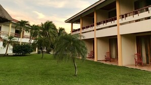 A hotel with a two-story structure, a covered outdoor seating area, and a well-maintained lawn with palm trees. - Nandel Beach Resort (La Cruz)