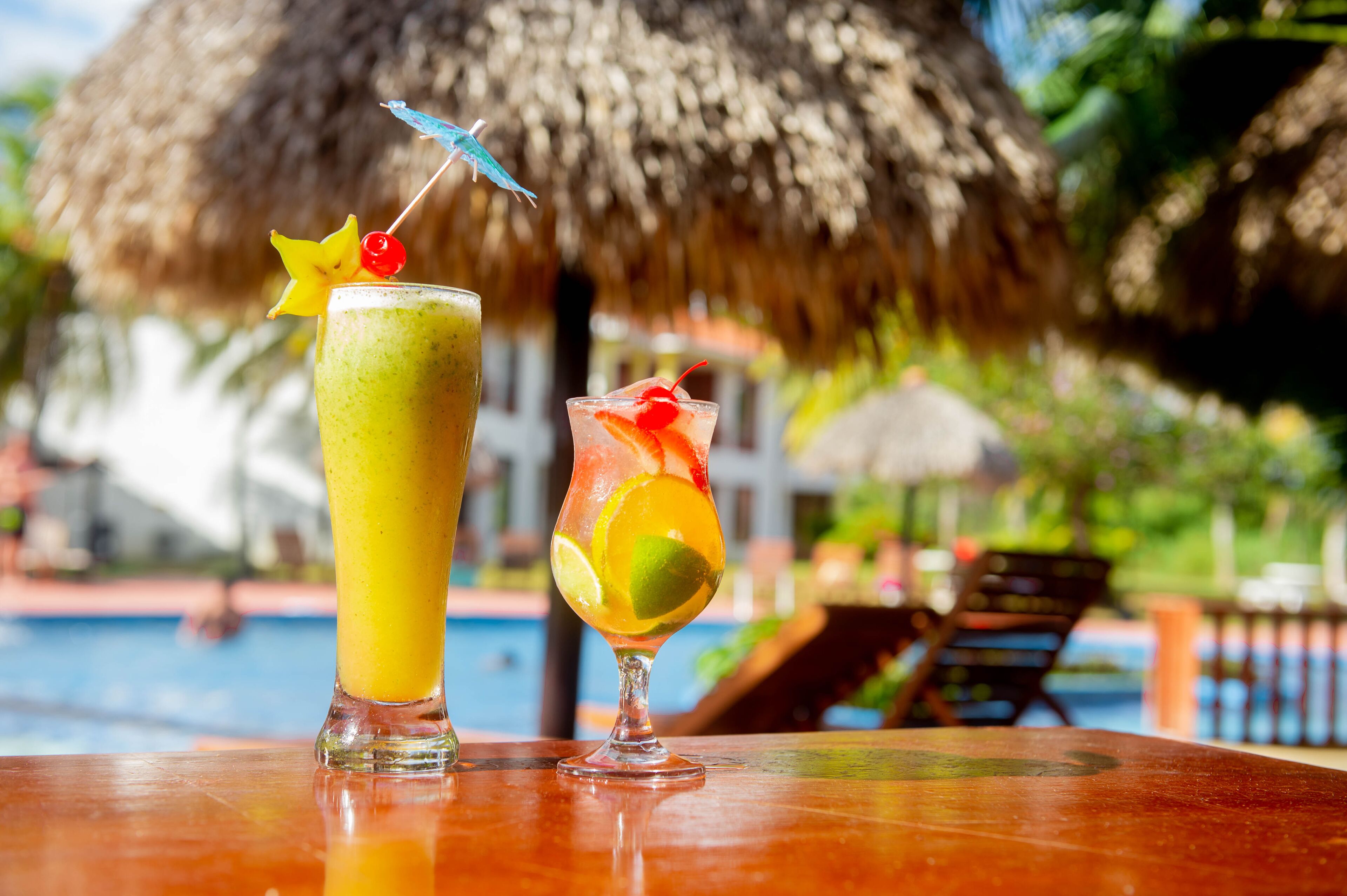 Due cocktail su un tavolo di legno, con una piscina e poltrone relax sullo sfondo.