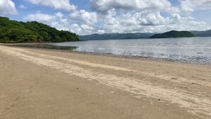 A beach with a sandy shore, calm water, and a forested hill in the background. - Nandel Beach Resort (La Cruz)