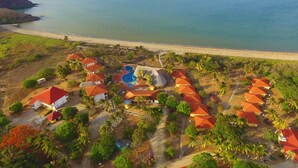 An aerial view of a resort with multiple bungalow-style buildings, a central pool area, and a beachside location. - Nandel Beach Resort (La Cruz)