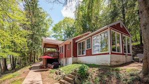 A cabin with a covered porch, a deck, and a view of the surrounding forest. - Charming Dog Friendly Cottage w/ Dock & Fire Pit (Mc Henry)