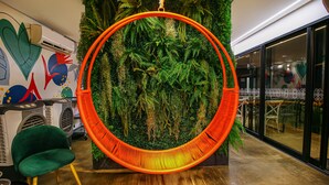 A room with a hanging orange hammock, a green chair, and a wall decorated with green foliage. - Pousada Flores do Carmo (Pirenópolis)