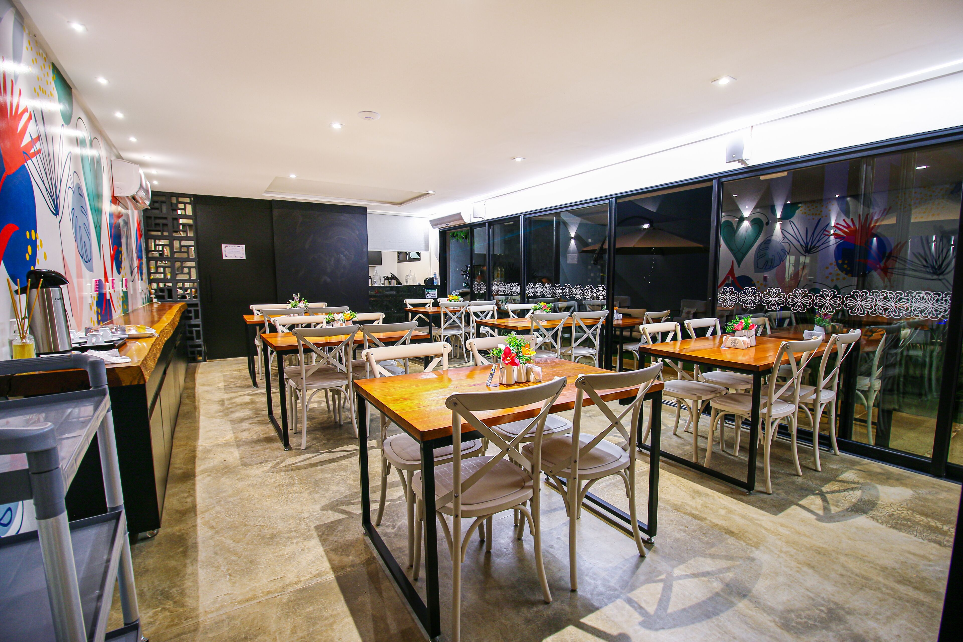 A modern restaurant with multiple dining tables and chairs, a kitchen area, and large windows with decorative glass panels.
