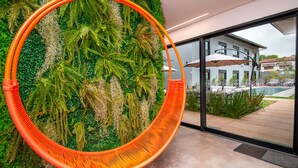 A hanging chair with an orange frame in front of a lush green wall with ferns and plants. - Pousada Flores do Carmo (Pirenópolis)