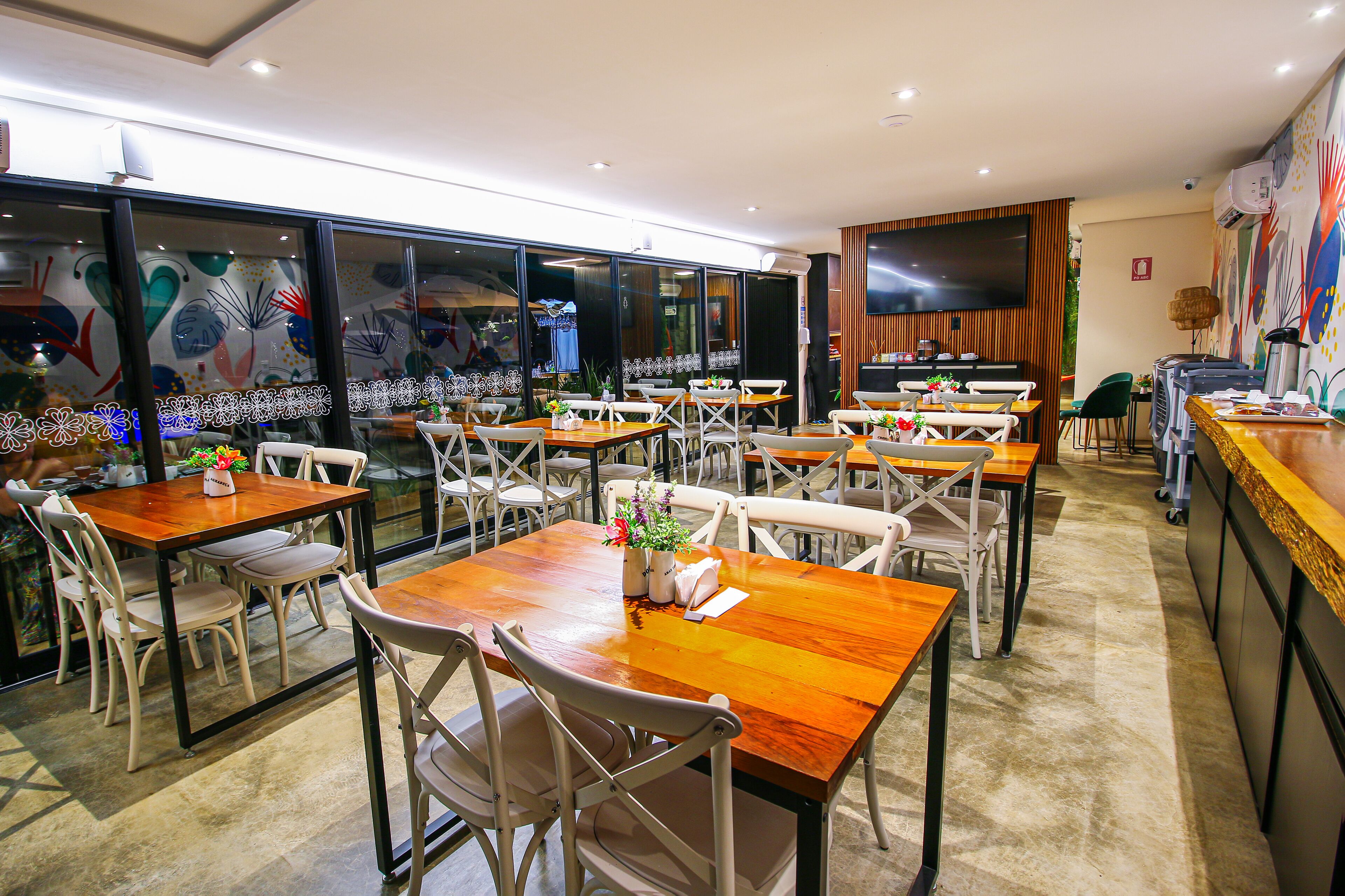 A restaurant with multiple tables and chairs, a large TV screen, and a decorative wall.