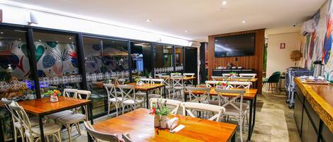 A restaurant with multiple tables and chairs, a large TV screen, and a decorative wall.