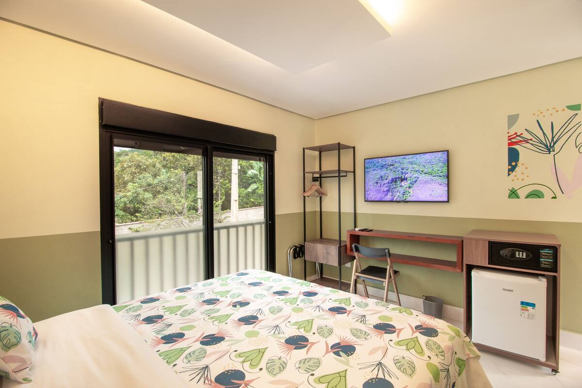 A hotel room with a bed, a desk with a computer, a television, and a small refrigerator.