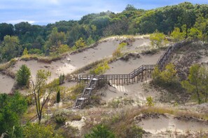A sandy beach with a wooden staircase leading up a dune, surrounded by greenery. - The "Pool Barn" w/Pool, Hot Tub,  Billiards & more near Indiana Dunes (Porter)