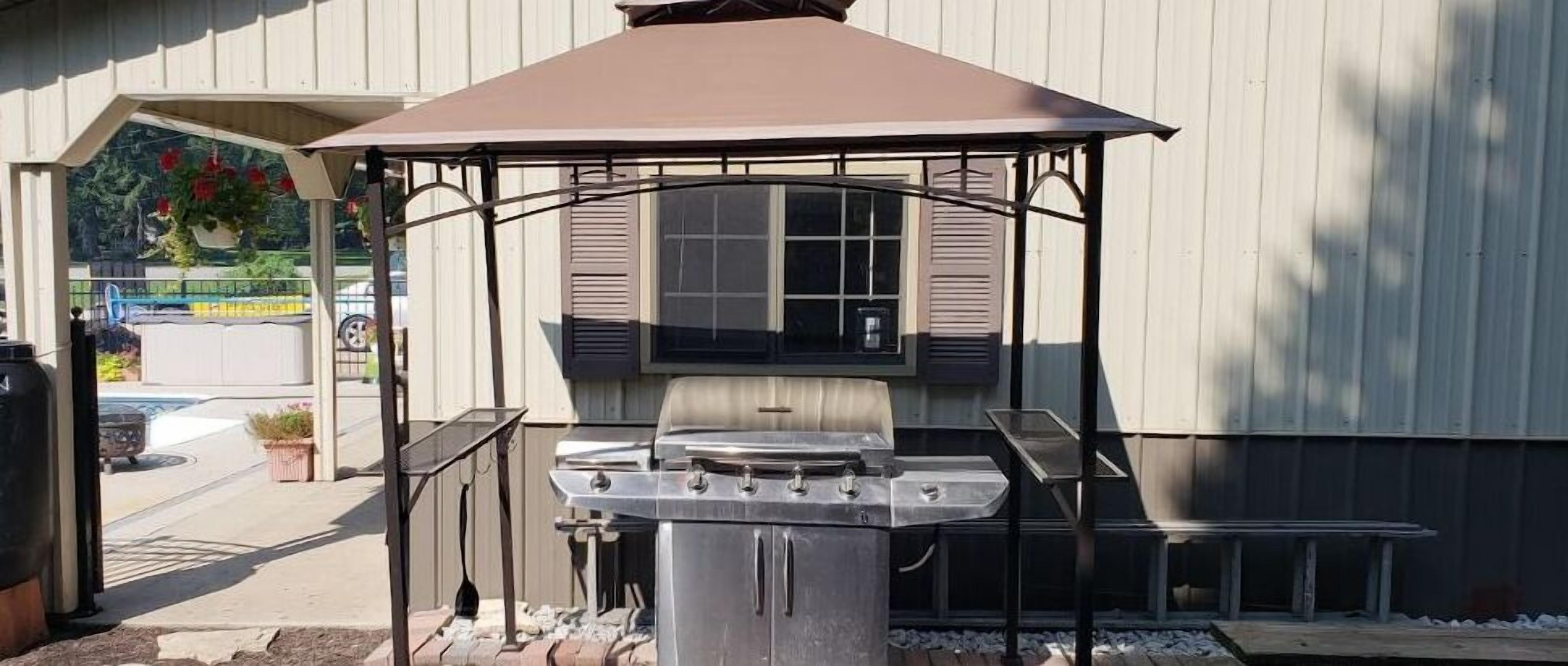 Un patio con una parrilla, mobiliario exterior y una estructura cubierta.
