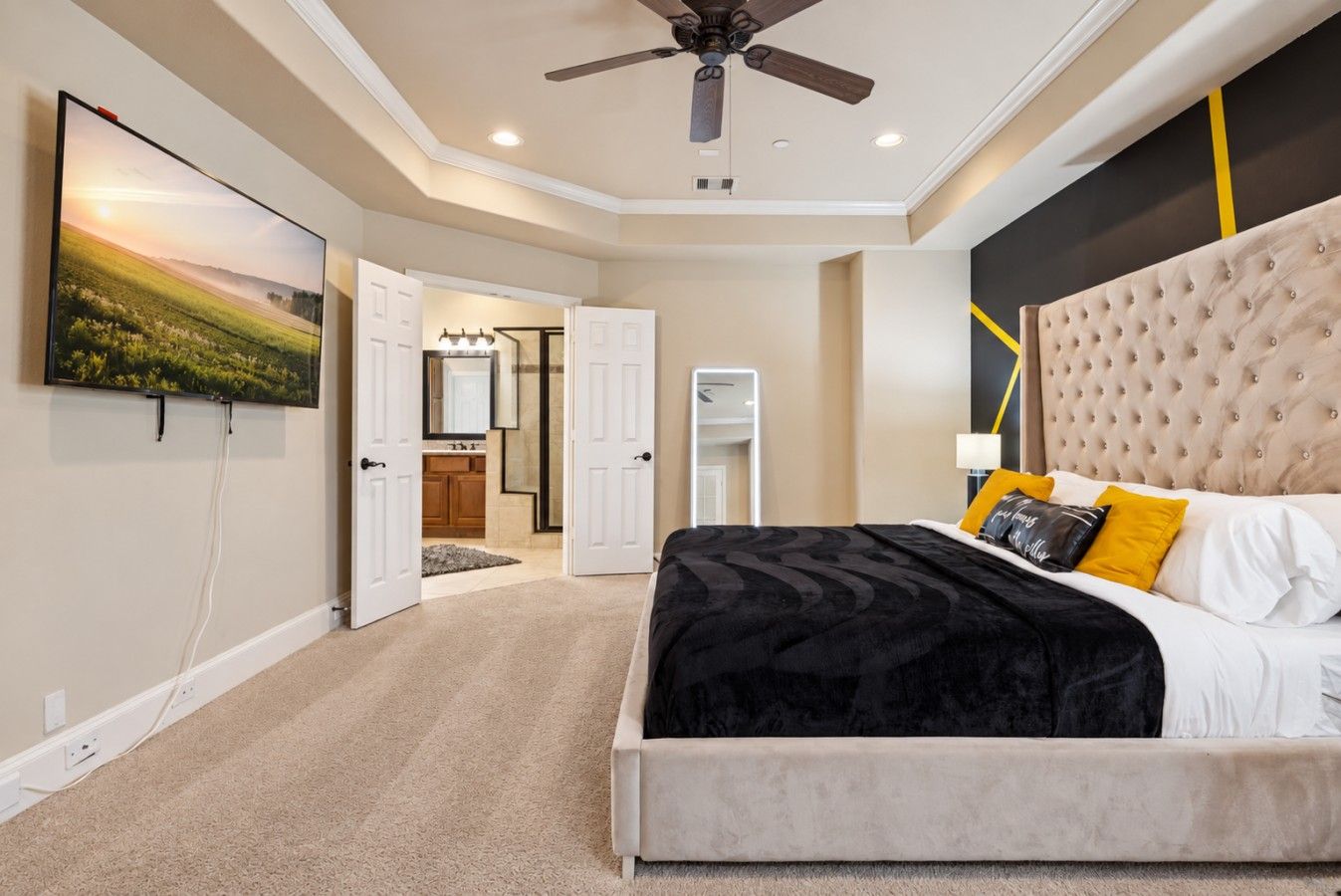 A bedroom with a large bed, a ceiling fan, and a view into the bathroom.
