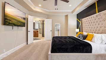 A bedroom with a large bed, a ceiling fan, and a view into the bathroom.