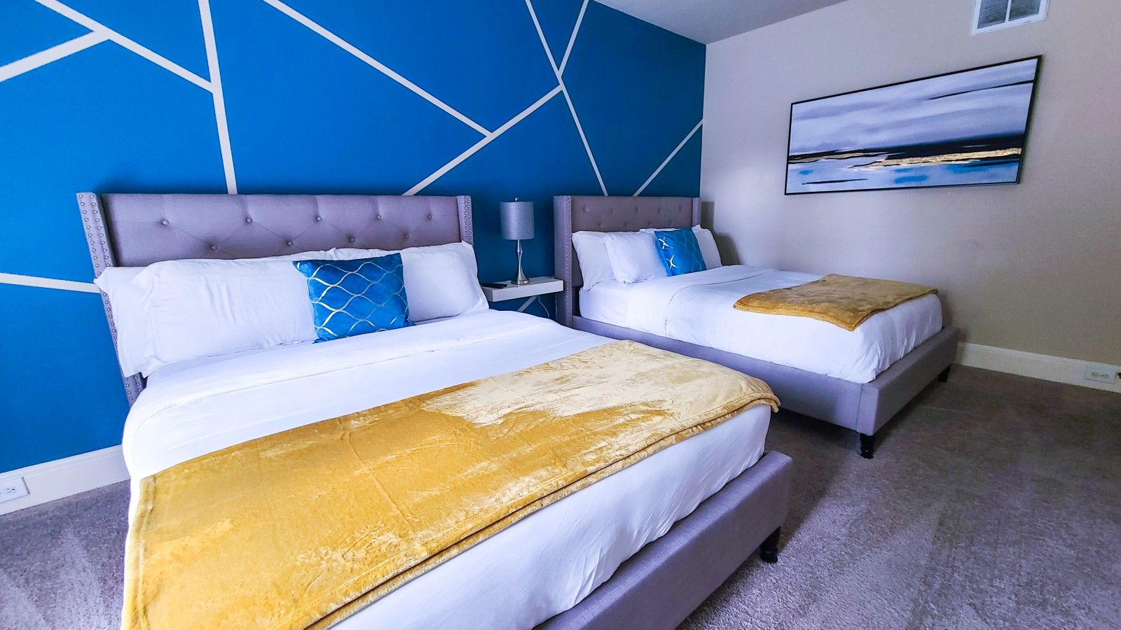 Habitación de hotel con dos camas, un diseño moderno en la pared azul y un cuadro colgado.