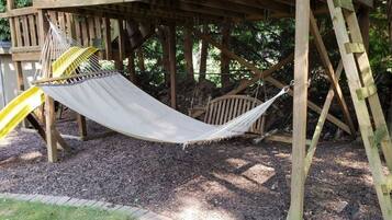 A hammock under a wooden structure with a slide.