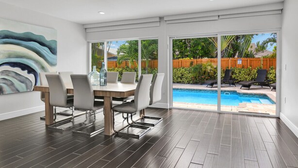 A modern dining area with a large table and chairs, a view of a swimming pool, and a large abstract painting on the wall. - Villa Coastal Cove Sparkling Pool Close to Beach BBQ En-Suite (Boca Raton)