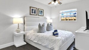 A bedroom with a bed, two nightstands, a ceiling fan, a window with a view, and framed artwork on the wall. - Villa Coastal Cove Sparkling Pool Close to Beach BBQ En-Suite (Boca Raton)