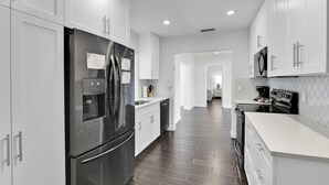 A modern kitchen with white cabinets, stainless steel appliances, and a dark wood floor. - Villa Coastal Cove Sparkling Pool Close to Beach BBQ En-Suite (Boca Raton)