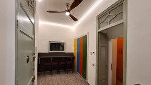 A hallway with a ceiling fan, a mirror, a bar area with chairs, and a door leading to another room.