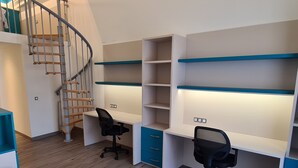 A modern bedroom with a wooden staircase, a bed, and two desks with chairs.