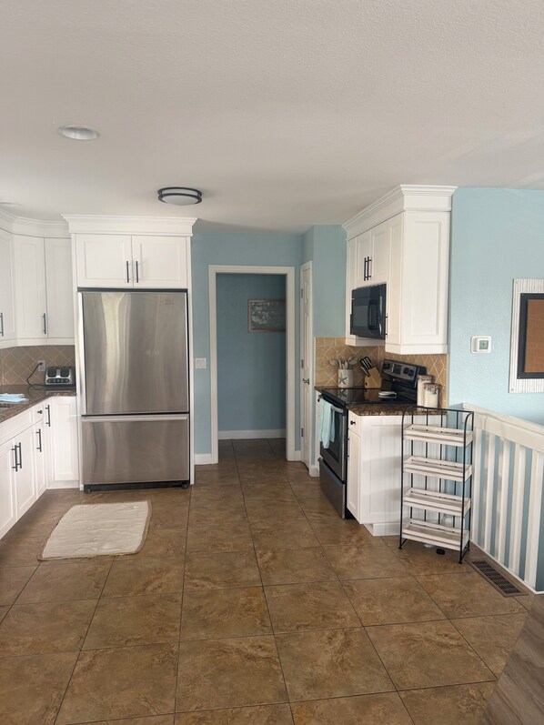 A kitchen with white cabinets, a stainless steel refrigerator, an oven, and a microwave.