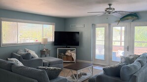 Un salon avec deux canapés gris, une table basse, un téléviseur à écran plat et un ventilateur de plafond.
