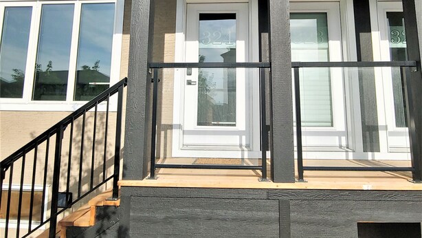 A two-story house with a covered porch, a visible door number, and a staircase leading to the entrance. - Serene 2 bedroom condo with balcony and lakeview plus Free Parking (Winnipeg)