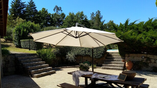 An outdoor patio with a wooden table and benches, a beige umbrella, and a stone staircase. - Casa de Campo, Casa do Batocal (Fataunços)