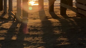 Estrutura de cais com vista para o oceano e o sol se pondo ao fundo.