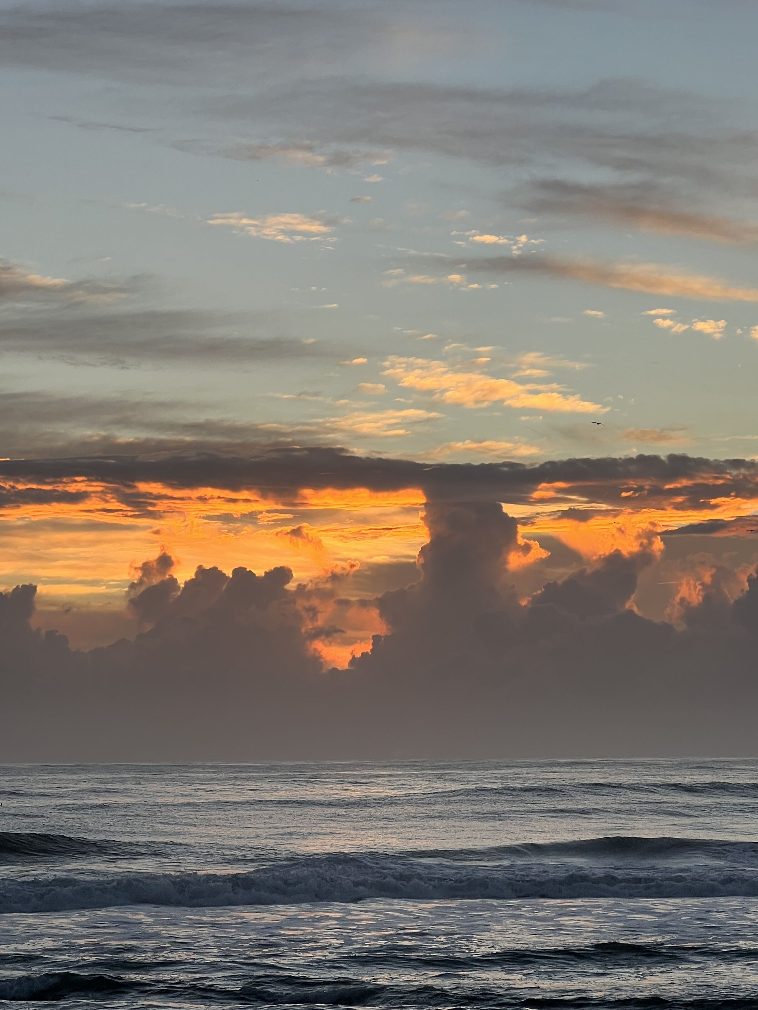 A sunset over the ocean with clouds and waves.