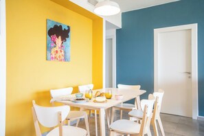 A dining area with a white table and chairs, a painting on the wall, and a door in the background.