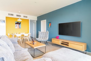 A modern living room with a sofa, a coffee table, a TV, and a dining area with chairs and a table.