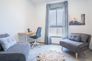 Een moderne kamer met twee grijze banken, een klein bureau, een stoel en een groot raam met gordijnen.