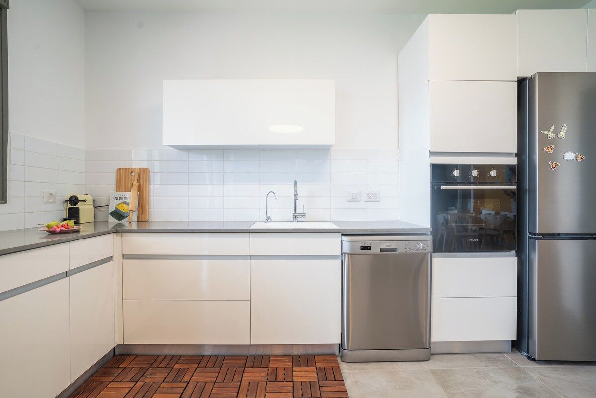 Een moderne keuken met witte kastjes, een RVS vaatwasser en een koelkast.