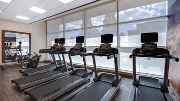 A gym with treadmills, stationary bikes, and a mirror reflecting exercise equipment.