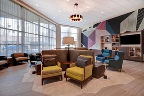 A modern hotel lobby with a seating area, large windows, a chandelier, and a wall with geometric patterns. - Home2 Suites BY Hilton Tucson Downtown (Tucson)