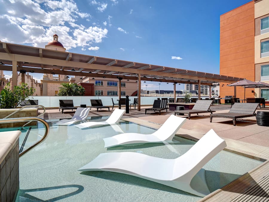 A rooftop pool area with lounge chairs and umbrellas, surrounded by buildings.