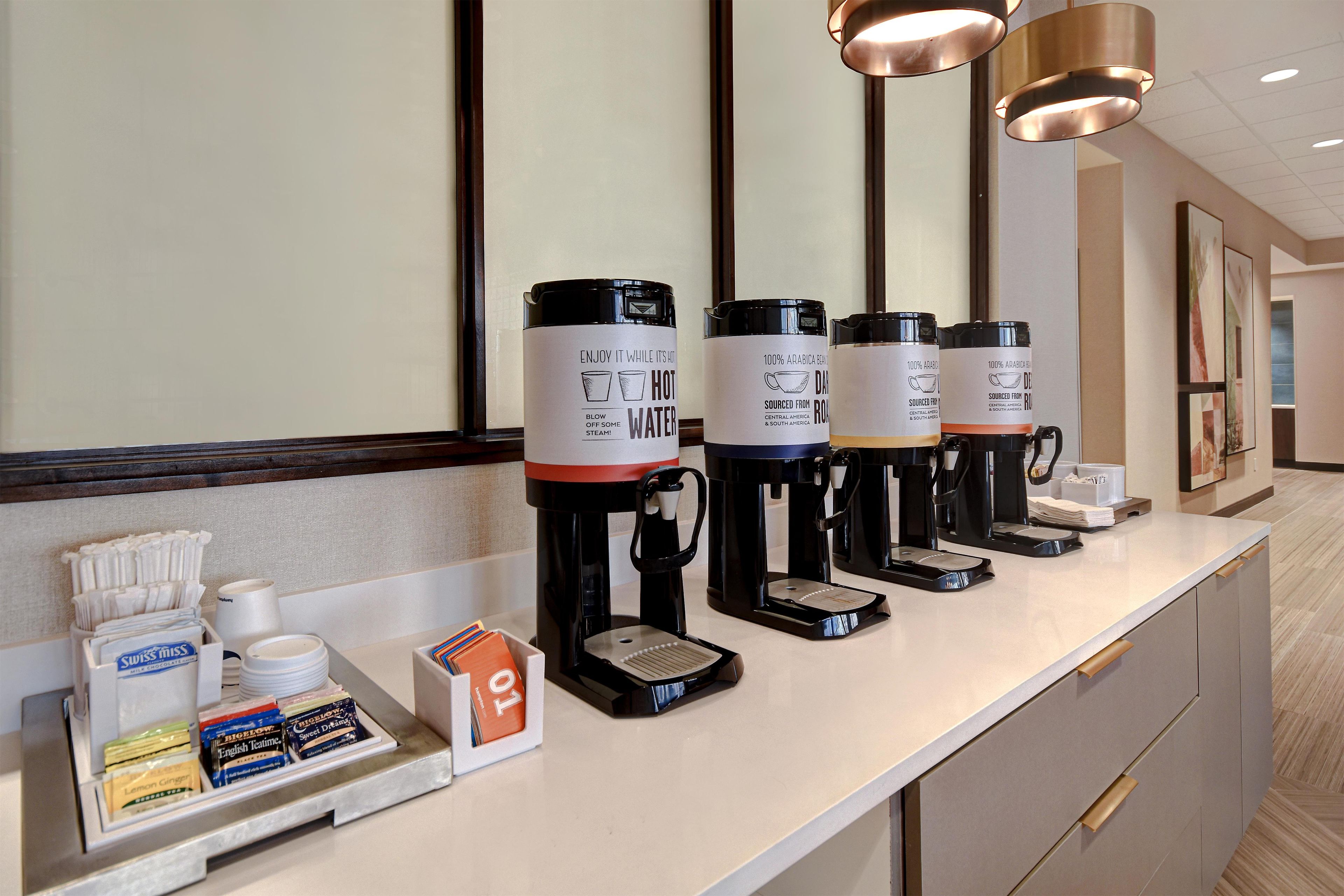 Un'area reception di un hotel con un angolo caffè dotato di diverse macchinette e una selezione di cialde per tè e caffè.