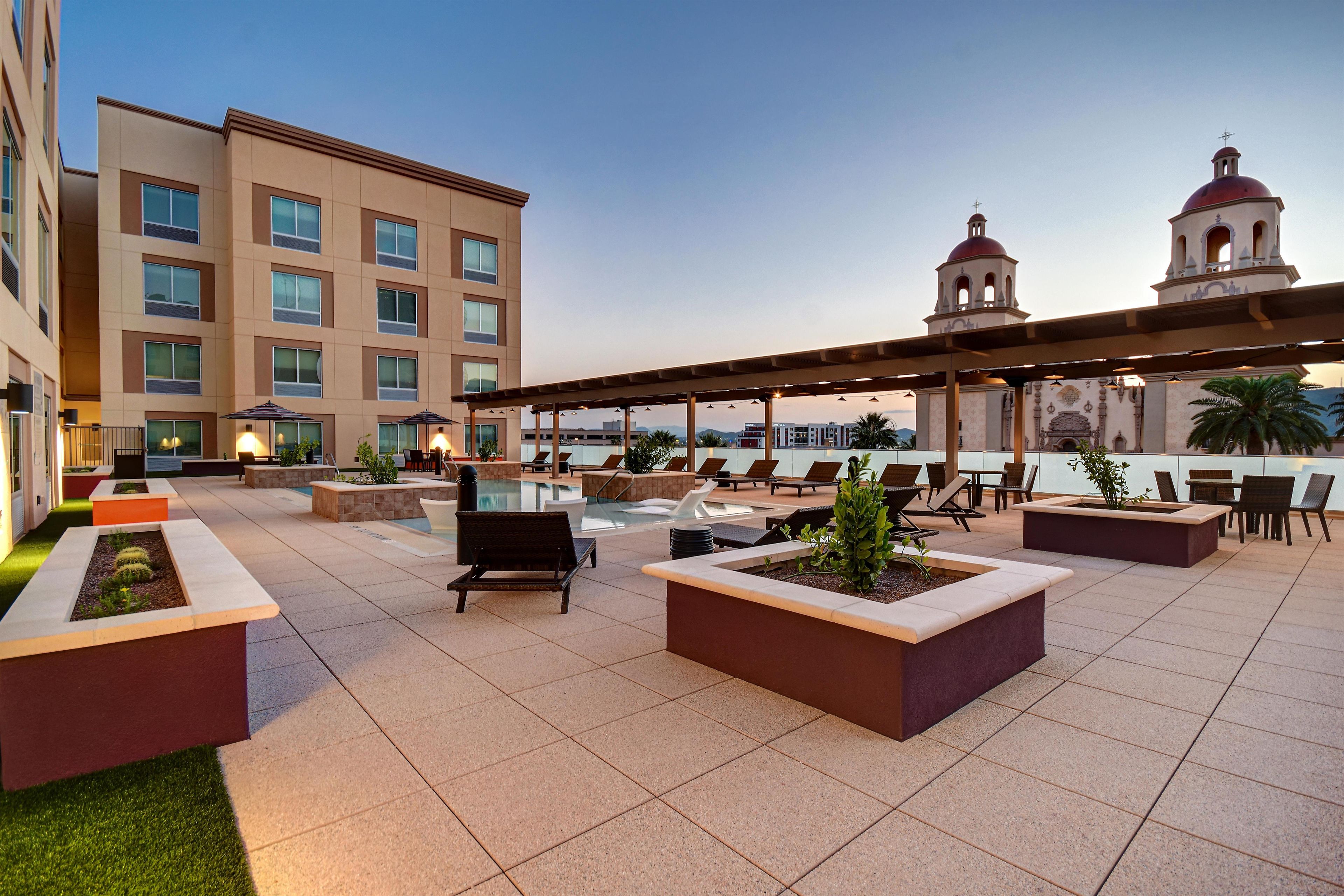 A rooftop terrace with outdoor seating, a pool, and a view of a building with a bell tower.