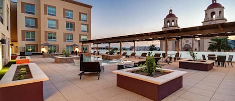 A rooftop terrace with outdoor seating, a pool, and a view of a building with a bell tower.