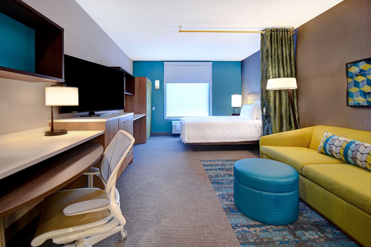 A hotel room with a bed, a desk with a TV, a sofa, and a chair.