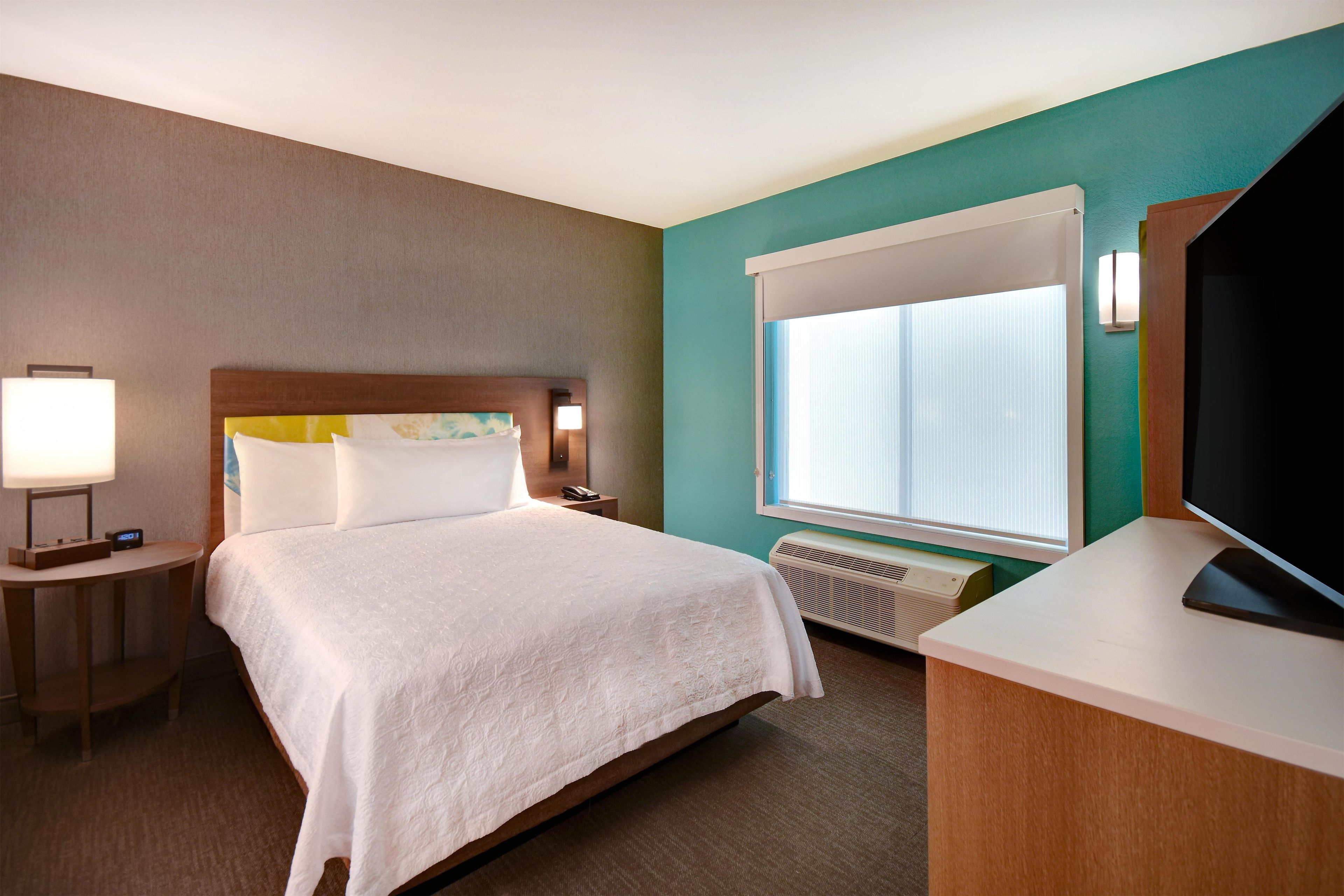 A hotel room with a bed, bedside table, lamp, and a large window.