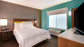 A hotel room with a bed, bedside table, lamp, and a large window.