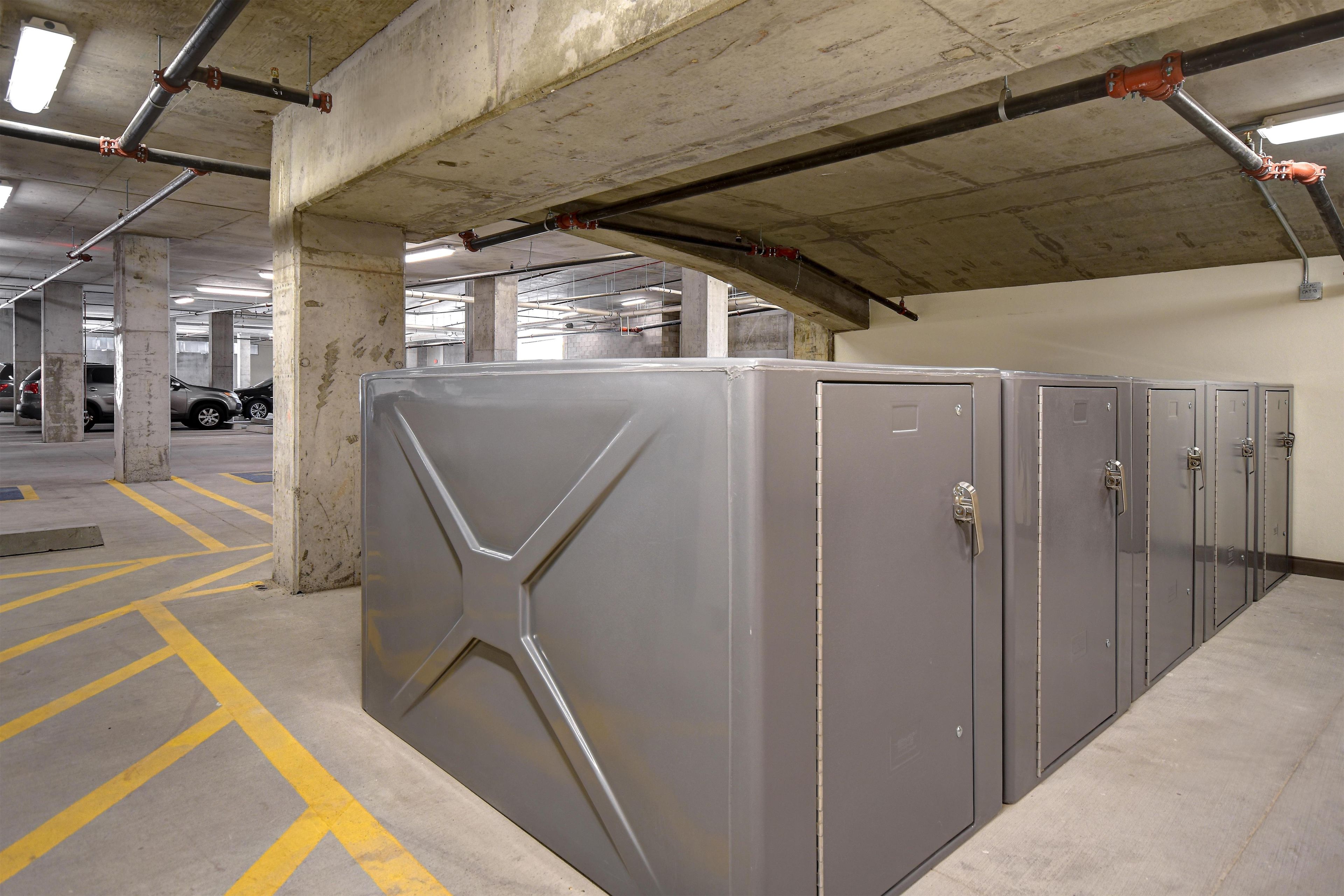 Un parking avec des piliers en béton, une grande porte métallique et une rangée de casiers métalliques.