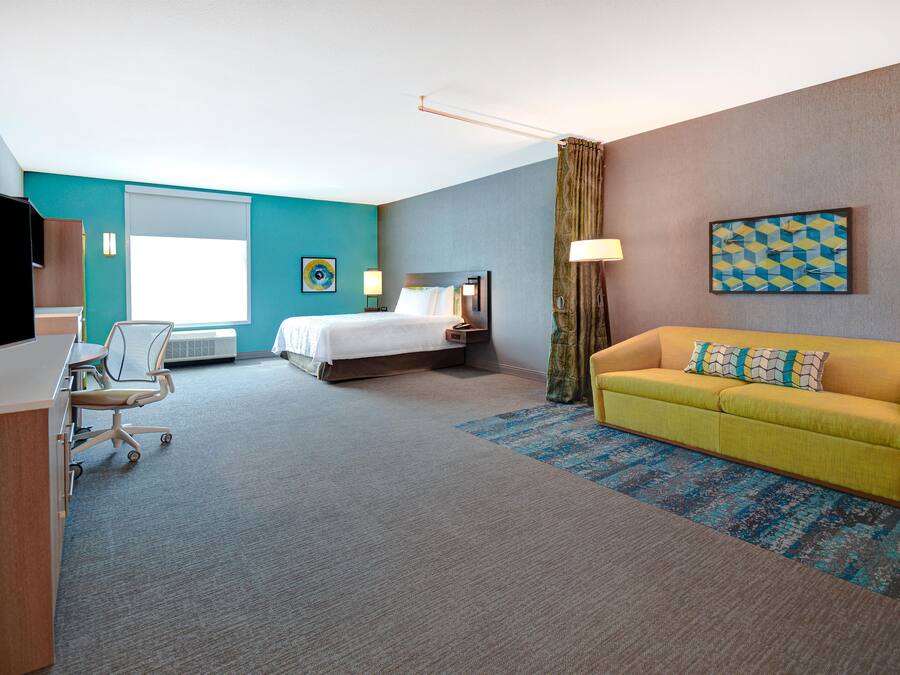 A hotel room with a bed, a desk with a chair, a sofa, a TV, and a window.